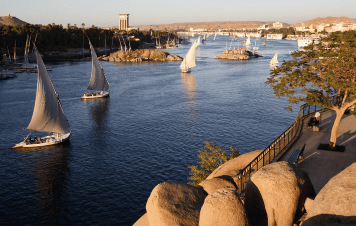 Feluccas sailing on the Nile River at sunset in Aswan, creating a picturesque scene with DMC Egypt.